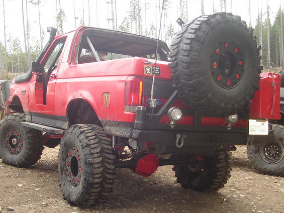 Red off-road SUV with large tires, snorkel, and spare tire on the back. Another vehicle is partially visible to the right