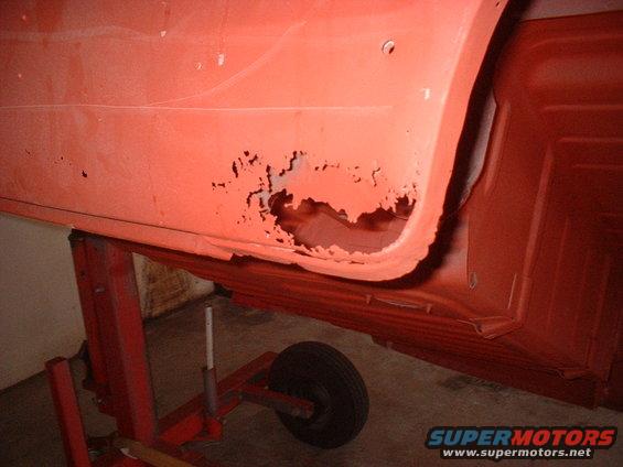 Rusted lower body panel on a vehicle supported by a red jack