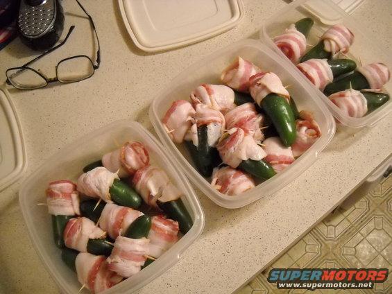 Jalapenos wrapped in bacon in plastic containers on a countertop