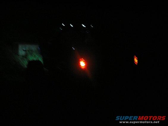 Red taillight glowing in the dark, with other lights in the distance