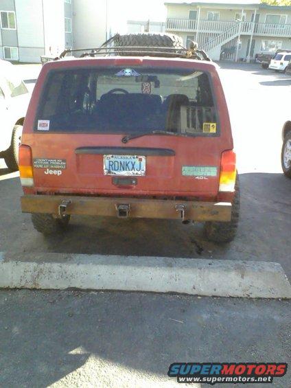 Red 1998 Jeep Cherokee with aftermarket bumper and roof rack, seen from the rear