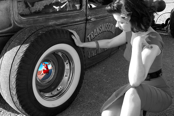 Woman in red dress touches whitewall tire on vintage car with 'TRANSMISSIONS UNLIMITED' text on door; reflection in wheel shows woman in red dress