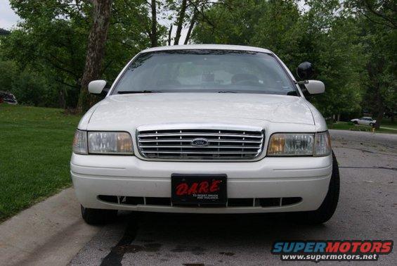 Front view of a white 1999 Ford Crown Victoria with a DARE license plate. Another car is visible in the background