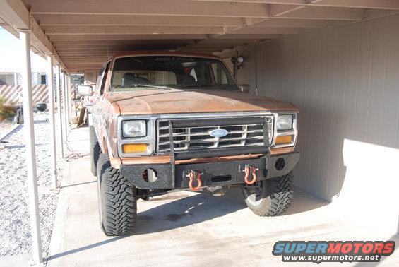 Brown Ford Bronco with aftermarket bumper and large tires parked under a carport