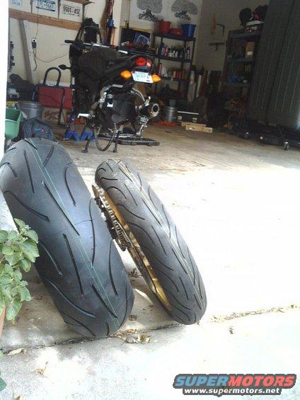 Two motorcycle tires, one new and one on a gold rim with a chain, in a garage