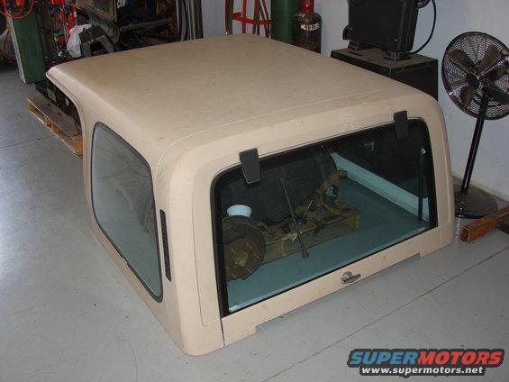 Tan Jeep hardtop with tinted windows, sitting indoors. Spare tire and tools visible inside