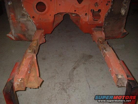 Orange painted car frame rails and firewall section, showing rust and repair welds