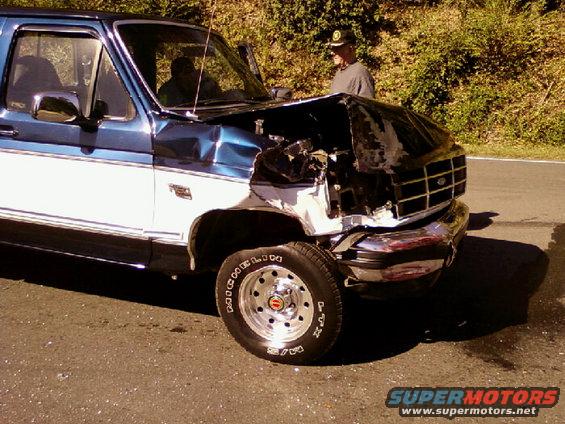 Front end collision damage on a blue and white Ford F-Series pickup truck. Grille and hood are heavily damaged