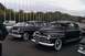 1991 Ford Crown Victoria - Two vintage black coupes are parked in an outdoor lot with many flagpoles in the background.