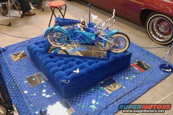 Blue custom motorcycle displayed on a plush blue platform with mirrors
