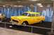 1991 Ford Crown Victoria - A yellow 1955 taxi cab is displayed in front of a New York City skyline backdrop, with another car visible to the left.