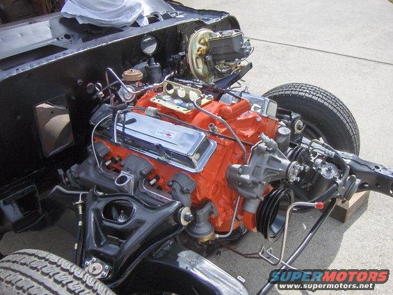 1970 Chevrolet V8 engine with orange block and chrome valve covers, partially installed in a chassis