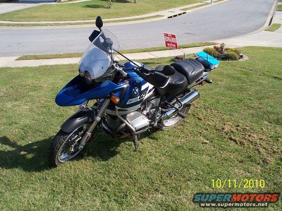 Blue BMW R1150GS motorcycle parked on grass, with a street and house in background. Date stamp 10/11/2010