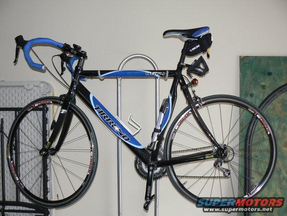 Black and blue Tirreno road bike mounted on a stand. It has drop handlebars and a water bottle cage