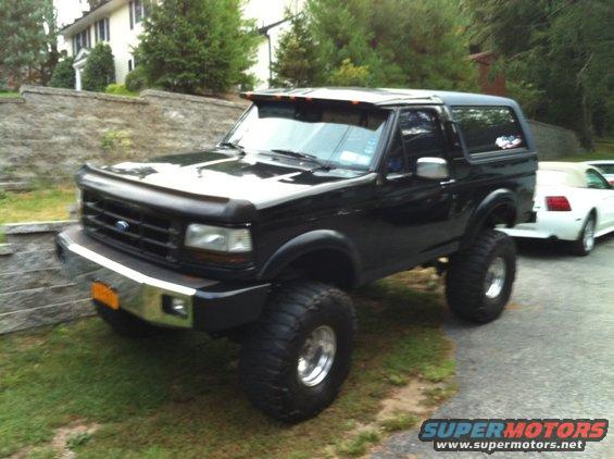 Lifted black Ford Bronco with aftermarket wheels and tires parked next to a white car