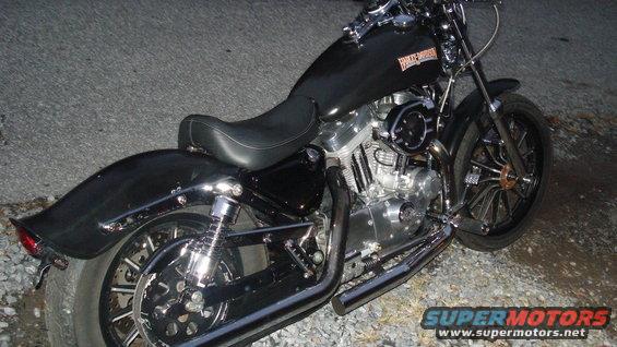 Black Harley-Davidson motorcycle parked on gravel. Shows the engine, seat, and rear wheel