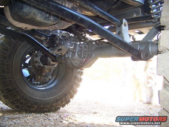Underside view of a vehicle's rear axle, differential, and suspension with a large tire