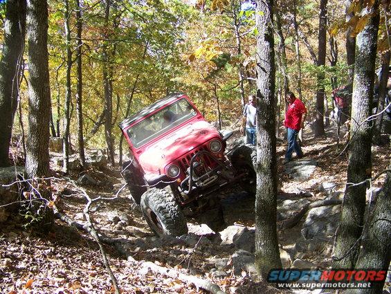 Red Jeep Wrangler navigating a rocky, wooded trail