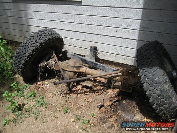 Front axle assembly with two large tires, leaning against a wall