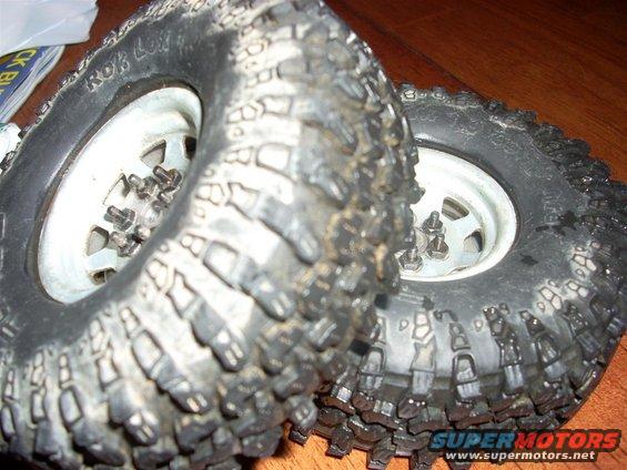 Two knobby off-road tires mounted on white rims, with visible lug nuts