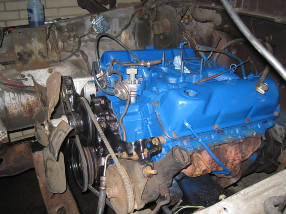 Engine block painted blue, showing fan, belts, and distributor cap. Some rust is visible on surrounding components