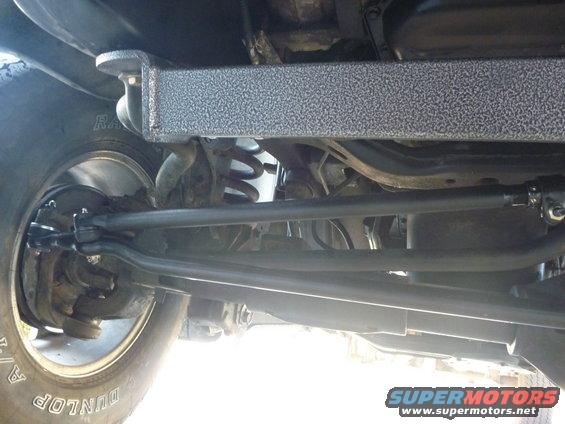 Undercarriage view of a vehicle's suspension and steering linkage, showing a tire and brake drum