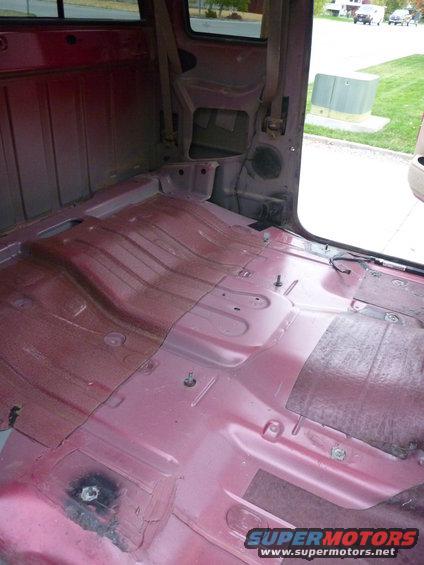 Interior of a red pickup truck, showing the bare floor and seatbelt anchors