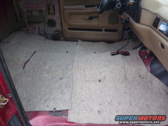 Interior of a red truck, showing the floor with carpet removed and exposed metal