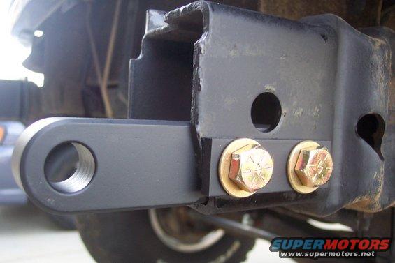 Trailer hitch receiver with two gold bolts attached to a black frame. A circular metal loop extends from the receiver