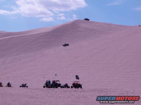 Off-road vehicles on sand dunes under a blue sky