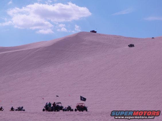 Off-road vehicles on sand dunes under a blue sky with clouds