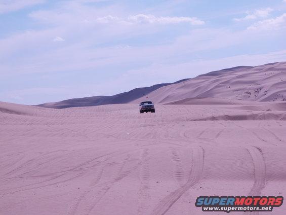 Truck driving on sand dunes under a cloudy sky