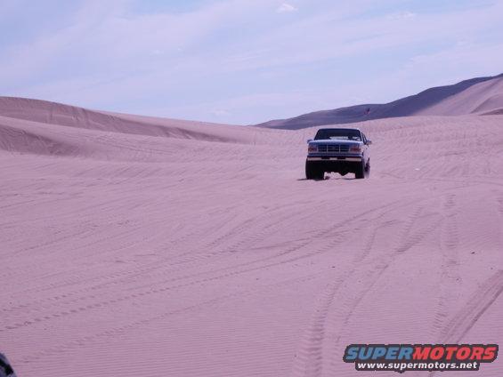 Blue pickup truck on sand dunes. Supermotors.net logo visible