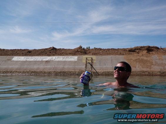 Man in water holding a can, with a concrete wall and dirt embankment behind him