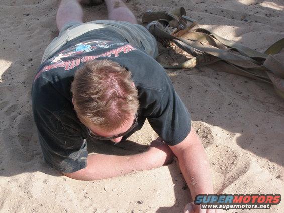Person in black t-shirt and shorts lying face down in sand, with a tow strap nearby