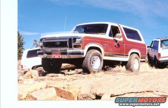 Red and white Ford Bronco parked on rocky terrain with another SUV behind it