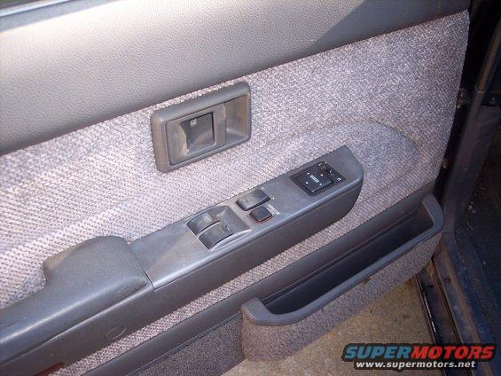 Car door panel with fabric upholstery, power window controls, and a door handle