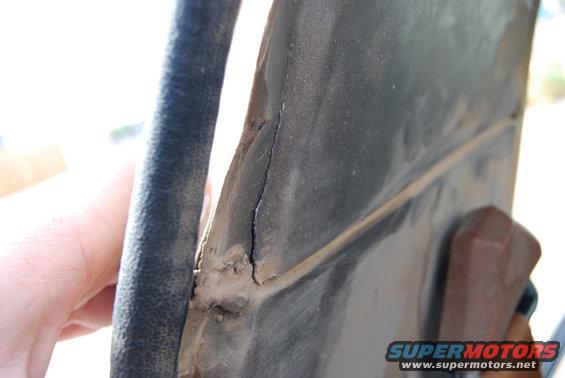 Close-up of a cracked metal panel with black rubber trim and a brown plastic piece. Supermotors.net logo visible
