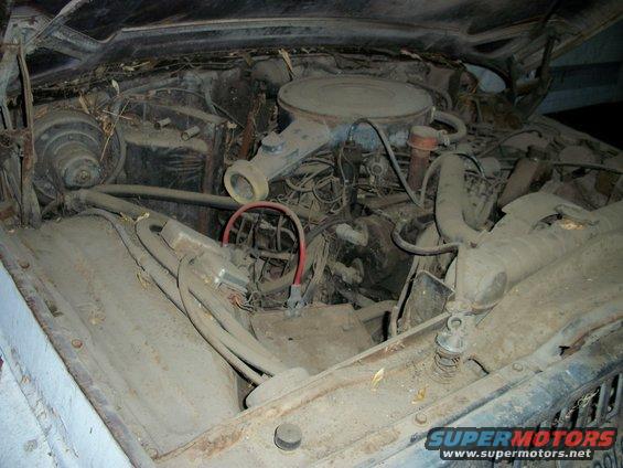 Dust-covered engine bay with V8 engine, air cleaner, and hoses visible. The hood is open