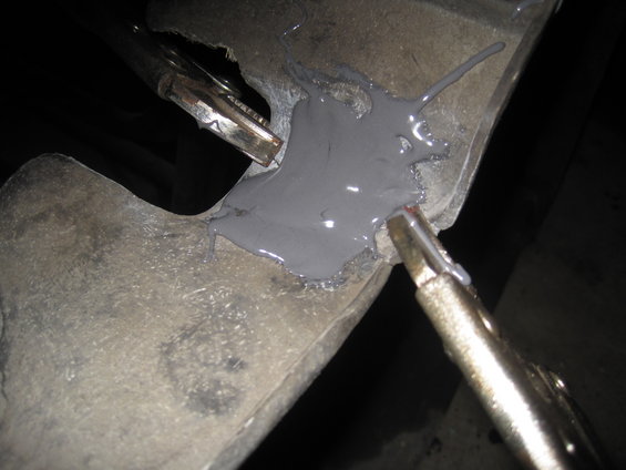 Close-up of a metal automotive part being repaired with grey putty and held by clamps
