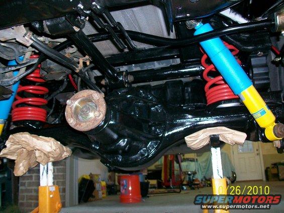 Rear axle assembly with red coil springs and blue/yellow Bilstein shock absorbers, supported by jack stands