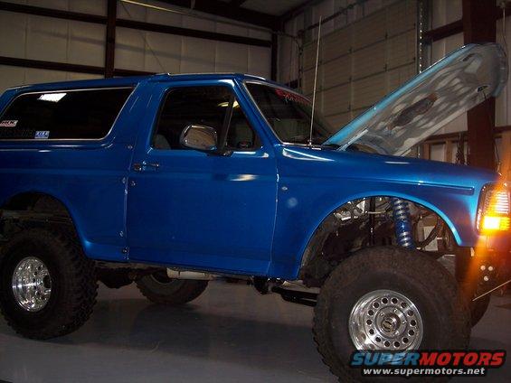 Blue Ford Bronco with hood open, showing engine components and suspension