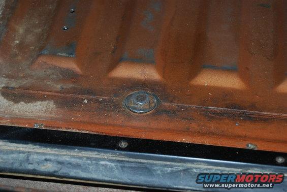 Close-up of a rusted orange metal panel with a hex bolt and black trim