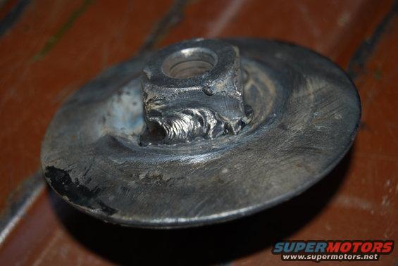 Close-up of a metal part with a nut welded to it. The metal shows signs of wear and tear