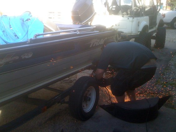 Person grinding on a boat trailer frame near a white SUV