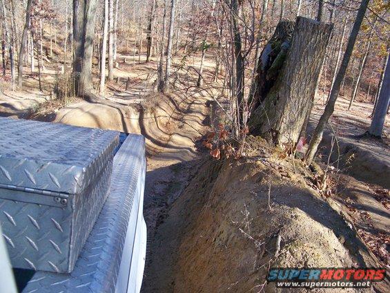 Diamond plate toolbox on a white truck bed, driving on a dirt trail through woods