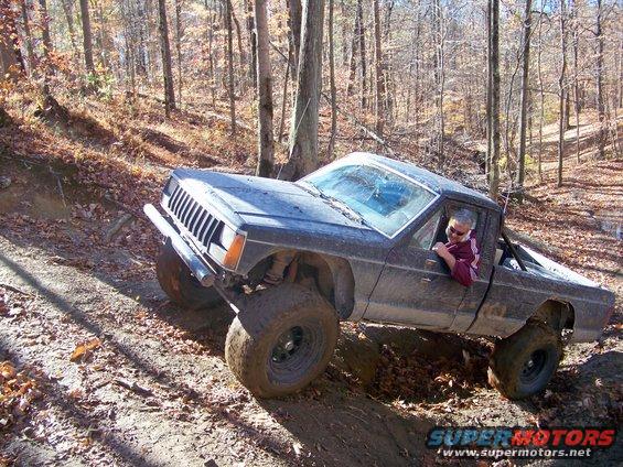 Dark gray Jeep Comanche pickup truck with large tires on a dirt trail