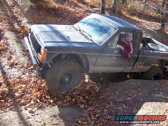 Dark pickup truck with lifted suspension navigating a muddy trail with fallen leaves