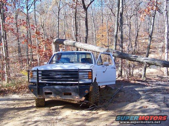 White 1987 Ford F-250 with open door, stuck on muddy trail