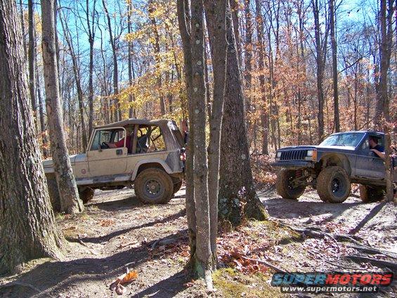 Two off-road Jeeps driving on a dirt path through a forest with fall foliage